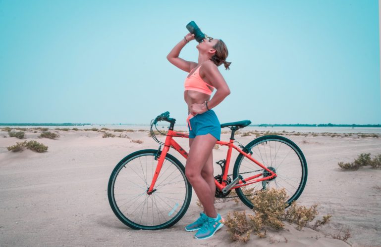 girl drinking water while resting on bicycle